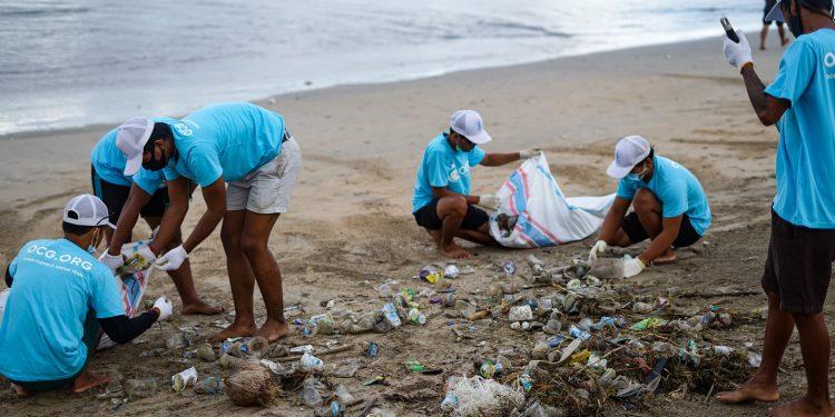 people on a beach wearing blue shirts picking up plastic waste