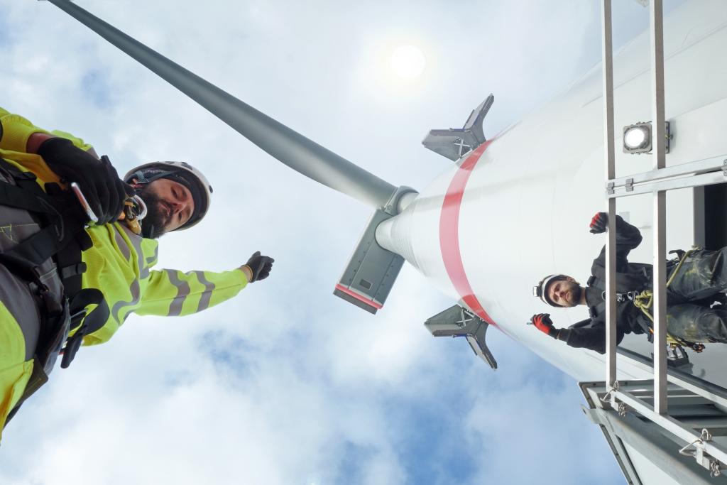 Two men in construction outfits at the bottom of a wind turbine, viewed from below