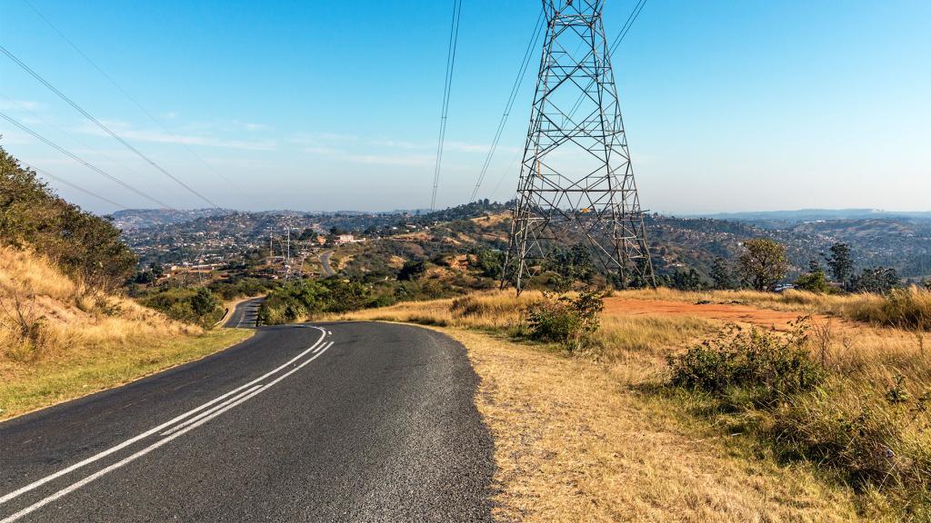 Power lines string alonside a road heading down rolling hills.