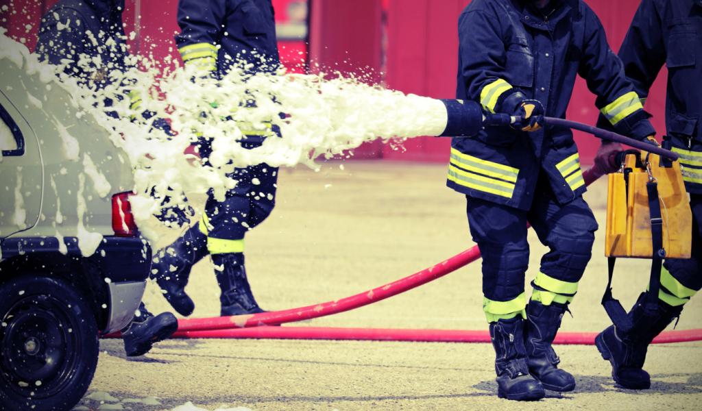 A firefighter holding a hose spraying foam onto a car