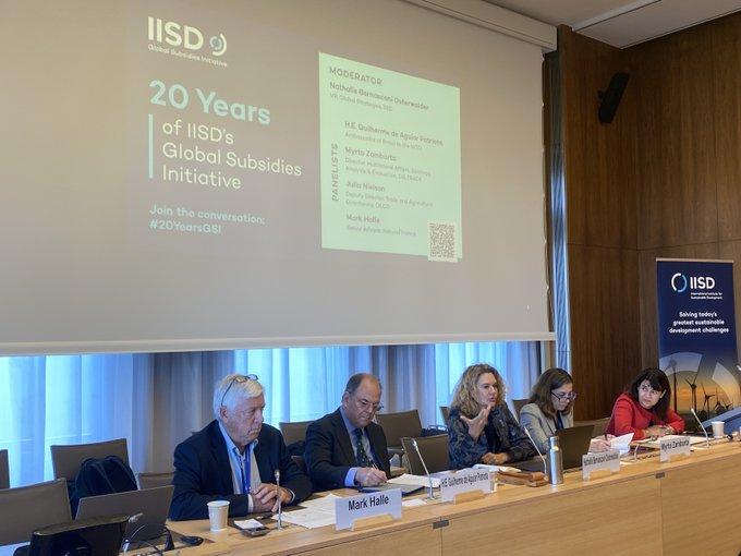 Five people sit on a panel at a conference event. A woman speaks into a microphone.
