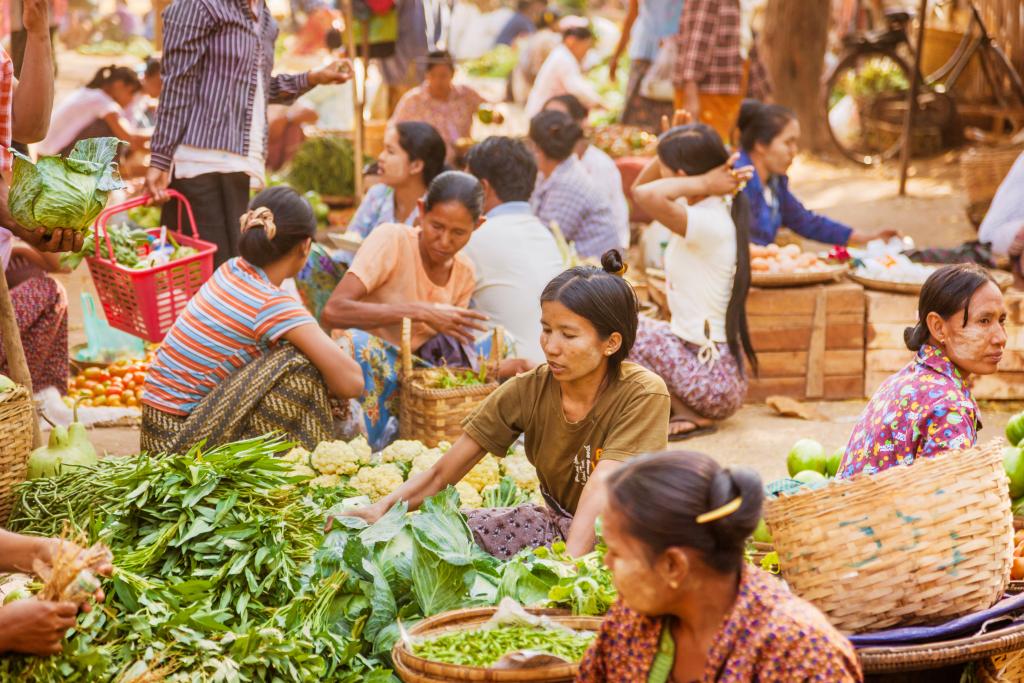 Women buy and sell produce at a market.