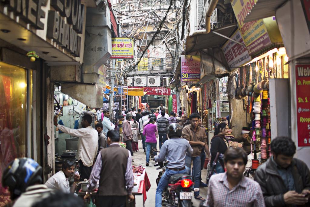 People walk through a narrow street lined with shops.