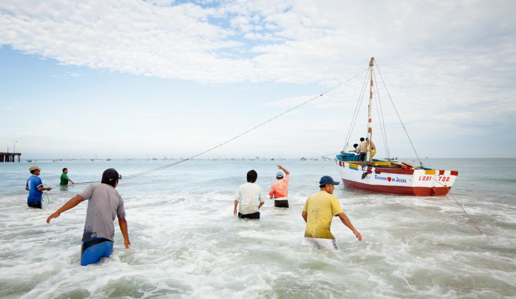 Men wade through water towards a small fishing boat.