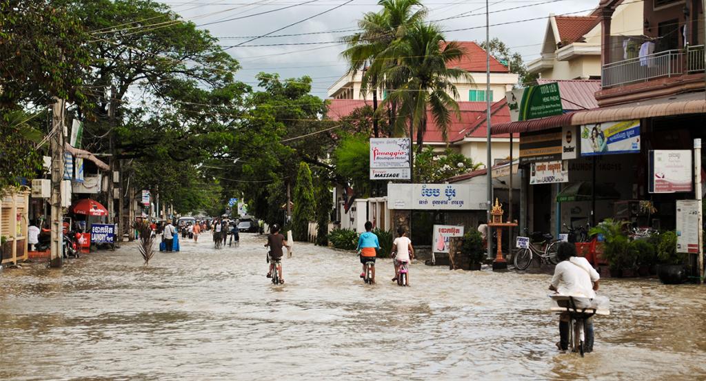 People walk and bike through a flooded city street.