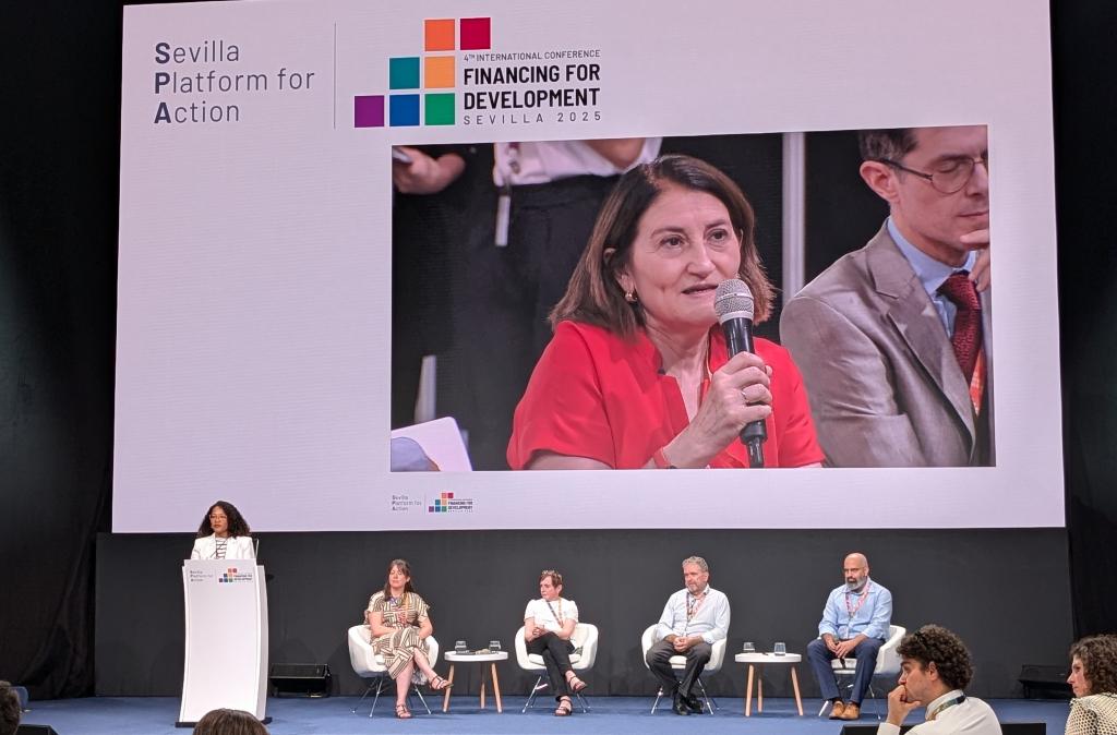 Panelists discuss on a stage, with a giant screen behind them showing someone asking a question