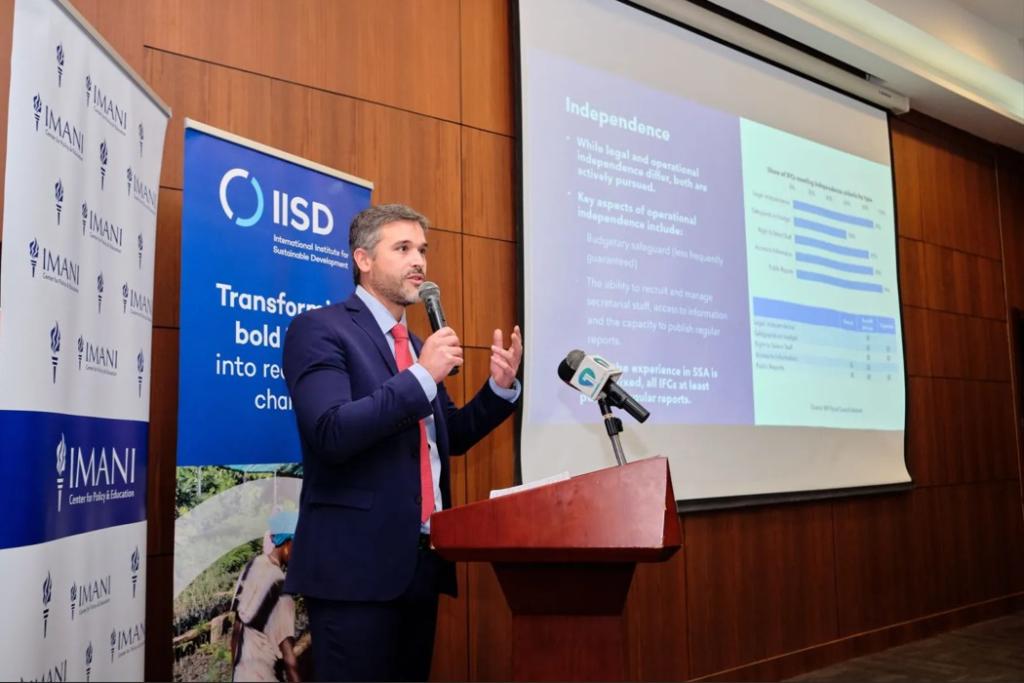A man is speaking to an audience with IMANI and IISD background, and a presentation behind him