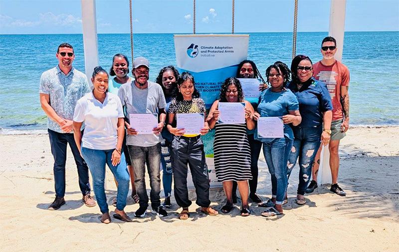 Group of Black people stands in on beach with their backs to the ocean holding certificates.