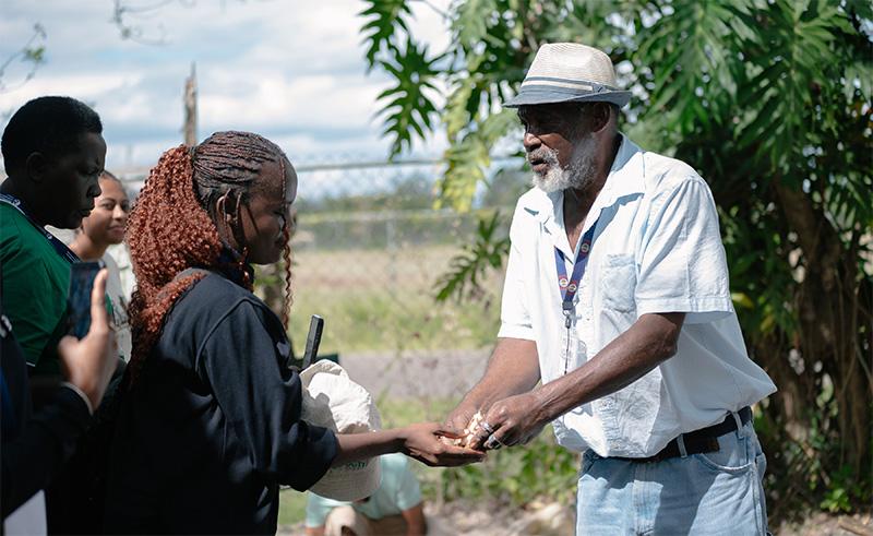Older Black man on the left hands something to young Black woman on the left.