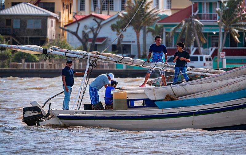 Five fishermen on a boat return to harbour in Belize City. Houses and palm trees are slightly blurry in the background.