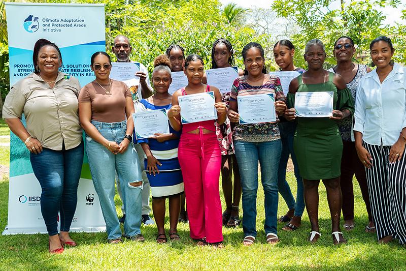 Group photo with participants holding certificates and standing on grass in front of trees.