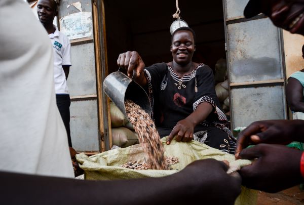 A woman pours dried beans into a bag in a market in Uganda, tied to story about COVID-19 spurring a hunger crisis