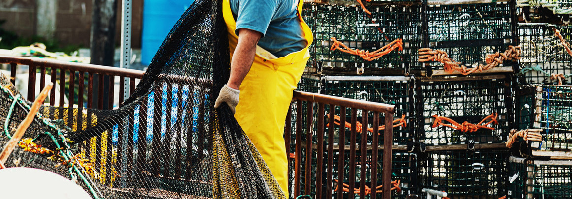 Fisher in yellow overalls hauls a fish net from the deck of a trawler.