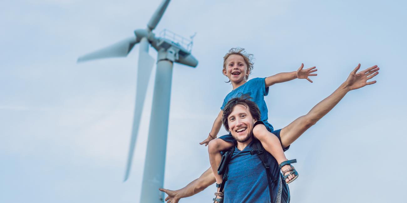 Kid on man's shoulders with arms out in front of wind turbine