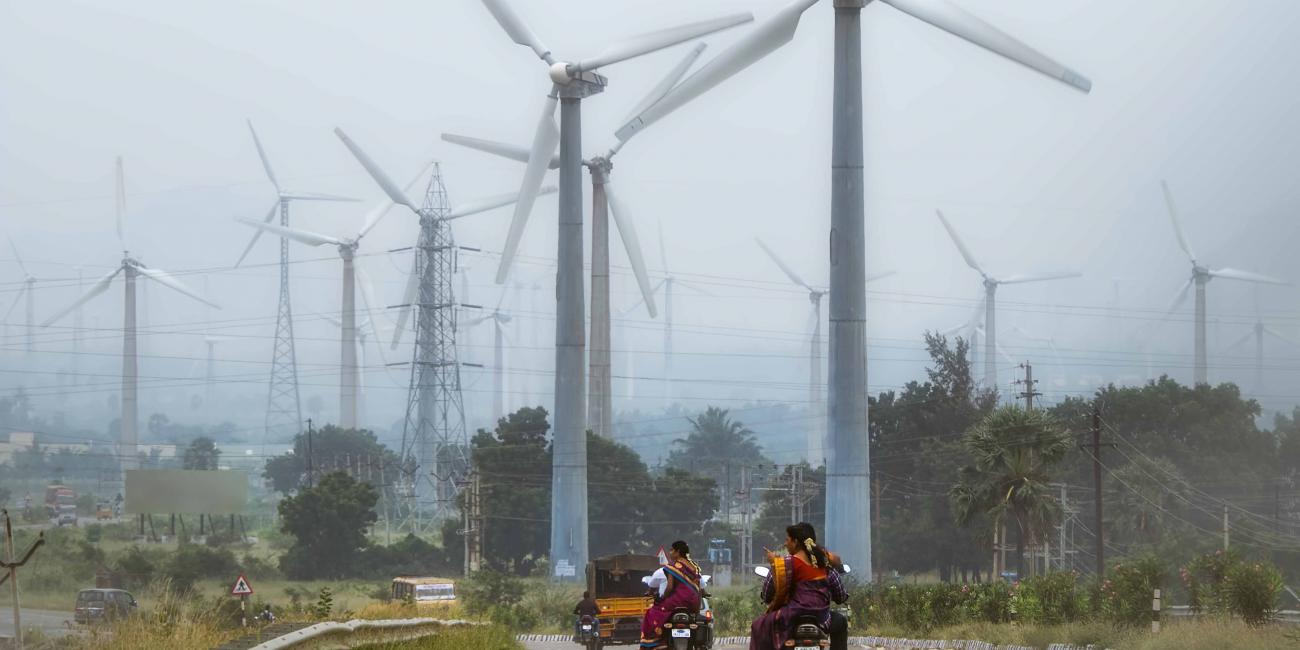 People on motorbikes drive toward wind turbines