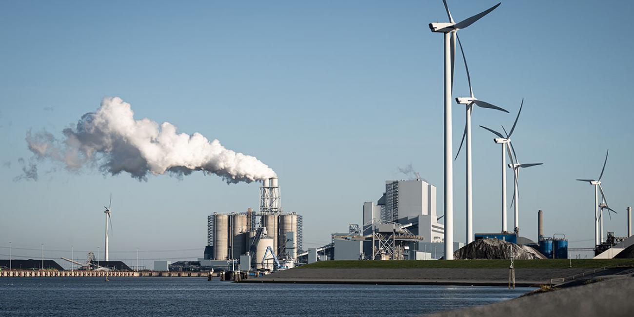 Wind turbines stand in front of a fossil fuel power station.
