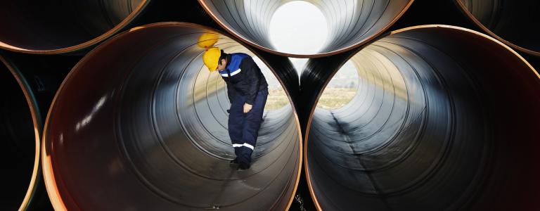 A construction worker bends over while walking through a large pipe