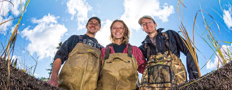 Three young scientists wearing overalls stand in a lake