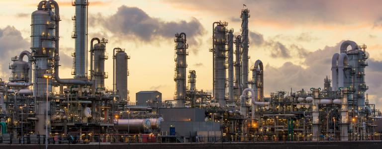 An oil refinery billows smoke against a dusk sky