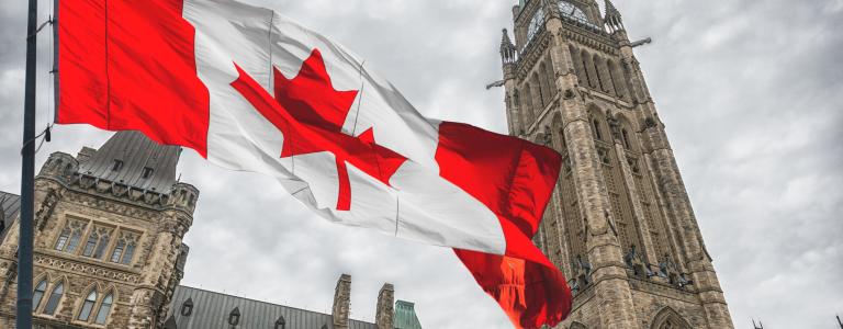 The Canadian flag flies in front of the parliament buildings on an overcast day